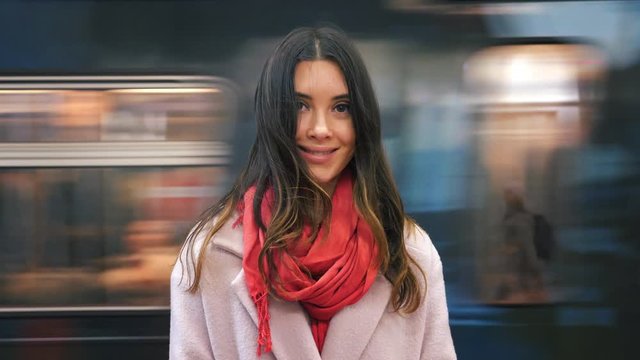 Beautiful happy young woman in red scarf smiling, looking at camera. Blurred subway train moving in background. Slow motion, 4K UHD.