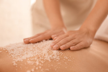 Young woman having body scrubbing procedure with sea salt in spa salon, closeup