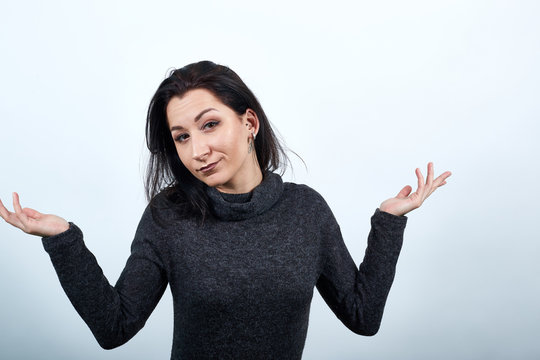 Beautiful caucasian young woman in fashion black sweater spreads hands, looking unhappy over isolated white background, Lifestyle concept