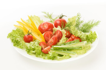 Fresh vegetables lie on the green leaves. Tomatoes, cucumbers, yellow peppers, lettuce isolated on a white background.