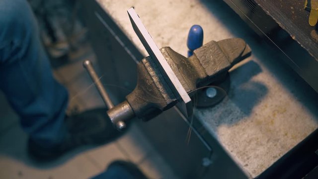 CU: young jeweler pulls long thin gold wire through tool fixed with bench vise clamp in workshop close upper view