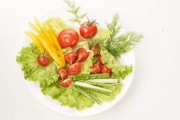 Fresh vegetables lie on the green leaves. Tomatoes, cucumbers, yellow peppers, lettuce isolated on a white background.