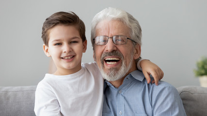 Head shot portrait little grandson embraces grey-haired elderly grandfather