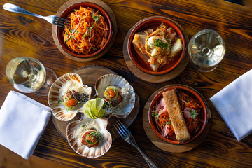 Tapas at a restaurant, carrots, scallops with red caviar and kimchi on a wooden table