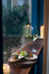 Scallops in a shell with red caviar in a restaurant, served with white wine, candles on background. wooden windowsill, blue walls