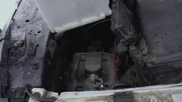Man removes Discharged automotive battery from car to fix or repair in winter. Malfunction or problem with automobile. Hood or bonnet raised up in daytime in parking. Closeup of lead-acid battery