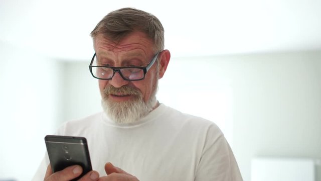 Close-up portrait of a handsome man with a mobile phone in his hands. Grandfather received a message from his grandson, a modern pensioner