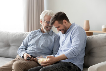 Elderly father grownup son laughing eating popcorn enjoy weekends together