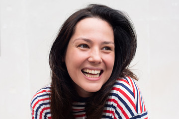 Close up happy young woman laughing by white background and looking away