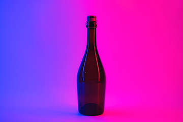 Uncorcked bottle of sparkling wine in neon background. Alcoholic beverage in vibrant lights, the concept of partying, holidays and drinking