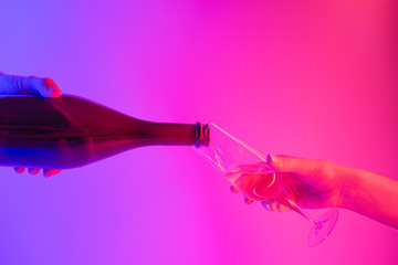Partying, celebration concept: pouring wine into a glass against bright neon background. Refreshing...