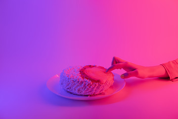 Sticking a finger into a cake. Female hand and birthday or party cake in bright vivid neon light