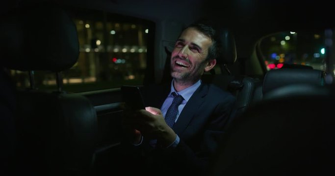 Slow motion of  handsome businessman using his mobile phone during  traveling in a modern car with a driver in center of the city by night. Shot in 8K. Concept of business, success, traveling, luxury 