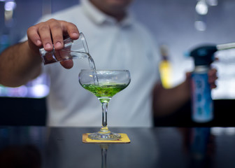 The bartender is lighting a cocktail, a cocktail is lit in a bar