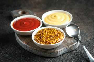 Set of popular sauces - mustard, ketchup and mayonnaise on a dark background. Free copy space..
