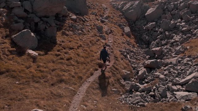 Aerial view following hiking man on arduous path in rocky mountain