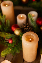close up of burning candles with spruce branches and christmas balls on wooden table