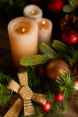 Fototapeta na wymiar close up of burning candles with spruce branches, bow and christmas balls on wooden table