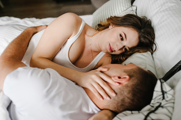 Woman hugging man in the bed, in a big bedroom. The Valentine's Day Concept. side view. Love story. Close up. Emotions of happiness.