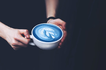 A cup of coffee in female hands with blue matcha latte.  in trendy blue toning. Main color trend for 2020 year.