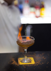 The bartender is lighting a cocktail, a cocktail is lit in a bar