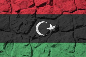 Libya flag depicted in paint colors on old stone wall closeup. Textured banner on rock wall...