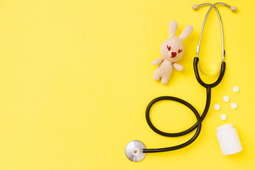 Children's toy amigurumi with stethoscope on yellow background with copy space. Child health concept. Top view, flat lay