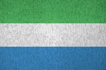 Sierra Leone flag depicted in bright paint colors on old relief plastering wall. Textured banner on...