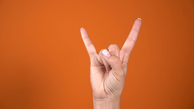 Closeup view of beautiful female hand showing Rock and Roll metal fingers horns gesture using fingers. Hand isolated on bright orange background. Real time 4k video footage.
