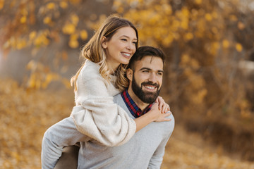 Fototapeta premium Young cheerful couple having fun while piggybacking in autumn day at the park