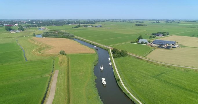 Descending Shot of a Row of Recreational Boats Across a Bendy River Leaving Dokkum with the Dutch Landscape, Friesland, Netherlands / Holland &ndash; 4K Drone Footage