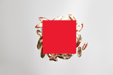 Festive minimalistic concept of red square frame template with gold leaves on gray background.
