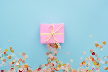top view of pink present with bow near colorful confetti on blue