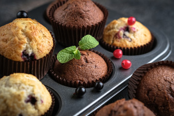 Various homemade muffins in a baking dish with berries, chocolate and mint on a dark background top view.