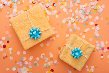 Fototapeta na wymiar top view of blue bows on gift boxes near confetti on orange