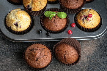 Various homemade muffins in a baking dish with berries, chocolate and mint on a dark background top view.