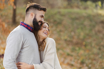 Fototapeta premium Smiling couple talking while walking embraced during autumn day in nature. Focus is on man
