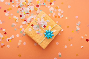 Obraz na płótnie Canvas top view of gift box with blue bow near confetti on orange