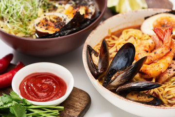 spicy seafood and meat ramen in bowls on white surface near ketchup