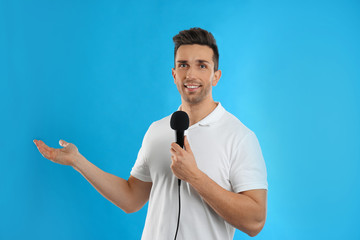 Young male journalist with microphone on blue background
