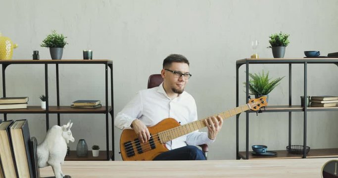 Man at work playing guitar for pleasure. Businessman is playing on guitar and enjoying it sitting in office during break. Guy practicing musical instrument. amera moves away from man. Music hobby.