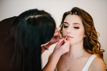 Makeup concept. The makeup artist makes the perfect makeup on the face and skin of the model. The stylist draws lips with a lip pencil. Beautiful woman. Close-up.