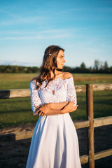 Fototapeta na wymiar boho wedding. Beautiful and stylish girl bride on a nature horse farm. One on the green field background. White lace dress, hair accessories.