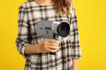 Woman with vintage video camera on yellow background, closeup