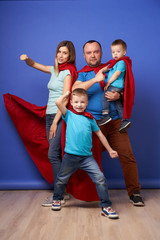 Young parents and children superheroes in red cloaks on blank blue background