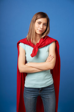 Girl in red superhero cloak standing on empty blue background