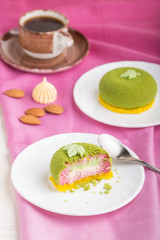 Green mousse cake with pistachio and strawberry cream on a pink background. side view, selective focus.