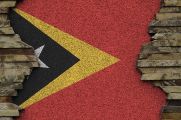 Timor Leste flag depicted in paint colors on old stone wall closeup. Textured banner on rock wall...