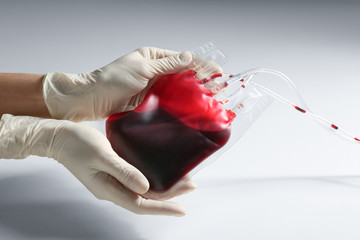 Woman holding blood for transfusion on light background, closeup. Donation concept