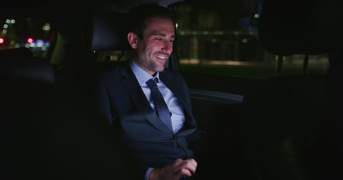Slow motion of  handsome businessman using his laptop during  traveling in a modern car with a driver in center of the city by night. Shot in 8K. Concept of business, success, traveling, luxury 